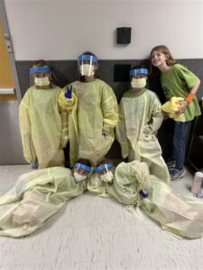 6 children posing in medical gowns with medical masks on.