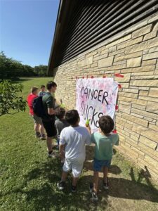A group of boys gathered around a poster that says "cancer sucks"