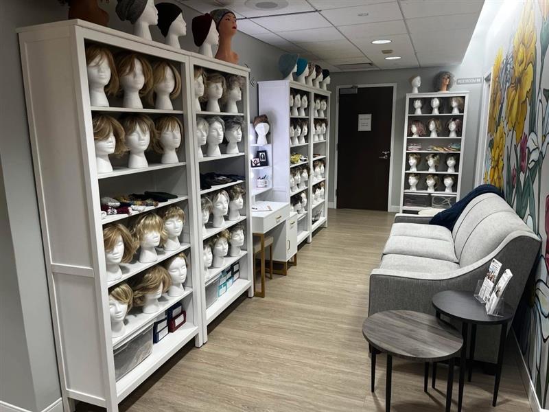 Image of a wig salon with wigs lined up on shelves and a couch along a wall.